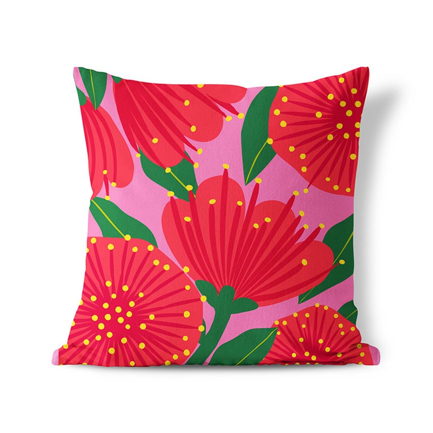 The Bright Botanical Pink Pohutukawa Cushion Cover features a bold polyester print of large red flowers with yellow dots and green leaves on a pink background. Ideal for both indoor and outdoor decor.