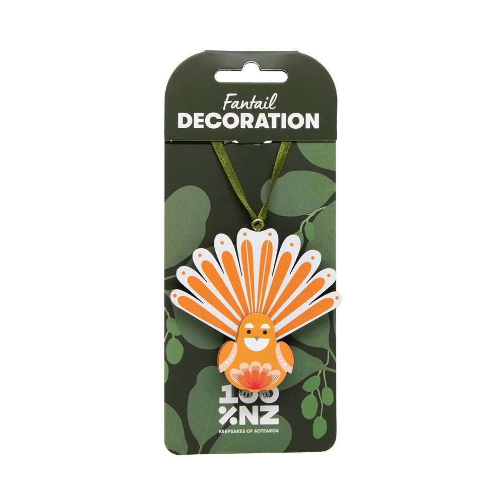 A vibrant orange and white fan-shaped Fantail Wooden Decoration is attached to a green ribbon, displayed on leafy-themed packaging with "100% NZ" at the bottom.