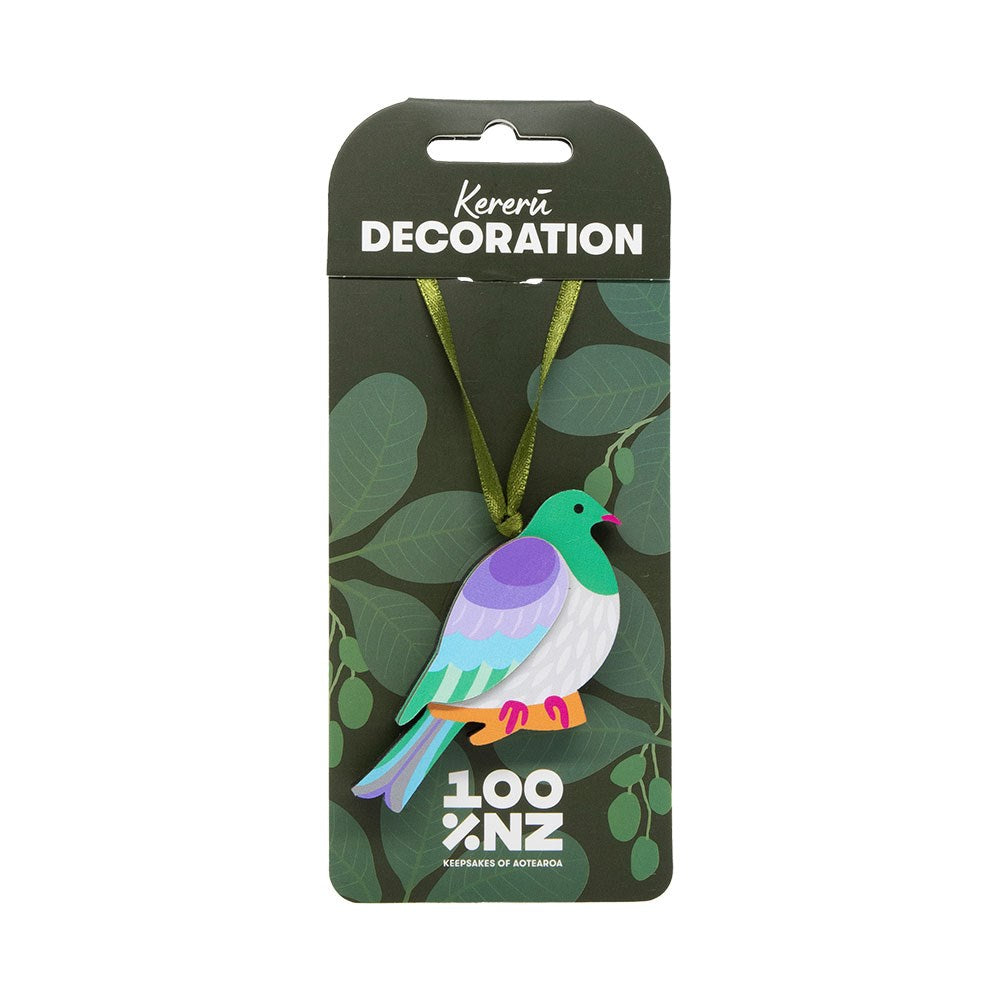 The Kereru Wooden Decoration is a flat, vibrant kererū bird with a green ribbon, attached to a green backing card labeled "Kereru Wooden Decoration" and "100% NZ," featuring leaf illustrations—ideal for a Kiwi Christmas.