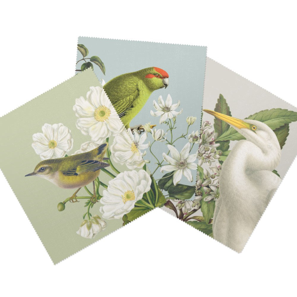 The Set of 3 Birds & Botanicals Collection Lens Cloths includes lens cloths featuring a yellow bird on white flowers, a green parrot on white blossoms, and a white heron with a yellow beak among leaves.