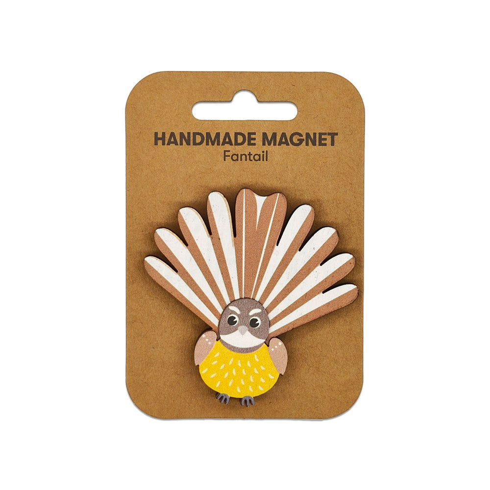 The Fantail Wooden Magnet is a handcrafted Kiwiana magnet shaped like a fantail, featuring a yellow body and white-brown fanned tail feathers, presented on brown cardboard backing labeled Handmade Magnet Fantail.
