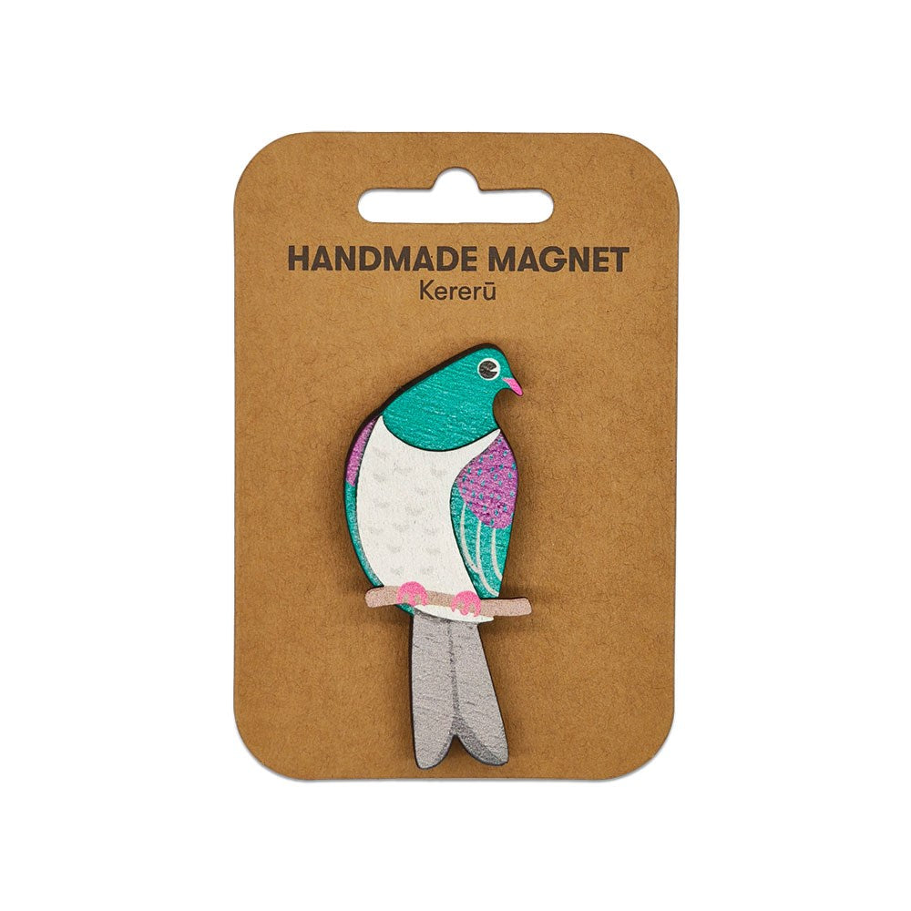 The Kereru Wooden Magnet is a handmade, hand-painted wooden magnet shaped like a kererū bird in green, white, and purple. Presented on a brown card labeled Handmade Magnet Kererū, it’s a charming Kiwiana addition to any collection.