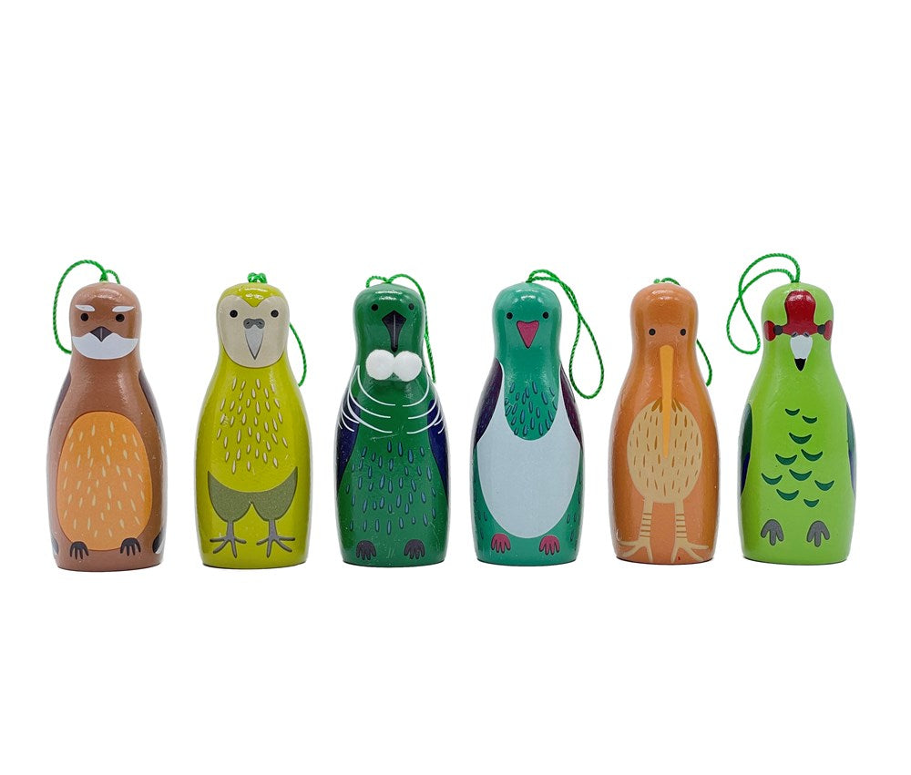 The Box of Native Bird Ornaments features six wooden pins painted as a beaver, owl, walrus, penguin, kiwi, and parrot with green string loops. Designed in New Zealand, this set makes a charming gift of Christmas ornaments.