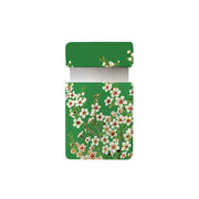 A rectangular green box with an open lid, decorated with Manuka flowers and green leaves, reveals the Manuka Flower Pocket Mirror inside. The floral design pops against a plain white background, evoking nature’s beauty.