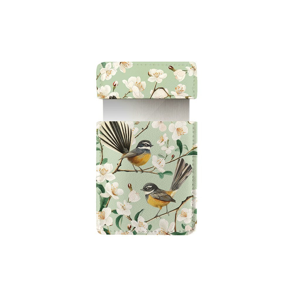 The Chatty Fantails Pocket Mirror has a rectangular vegan leather pouch with a flap, showing two brown, black, and white birds on flowering branches with white petals and yellow centers set against a light green background.