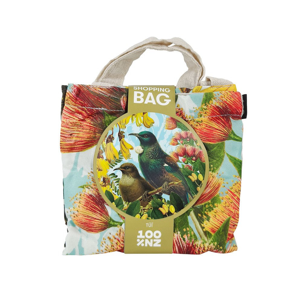 The Botanical Tui Shopping Bag is a lightweight, reusable tote featuring two birds among vibrant red and yellow flowers with green leaves, beige handles, and a “Shopping Bag” label by New Zealand brand 100% NZ. Ideal for affordable shopping needs.