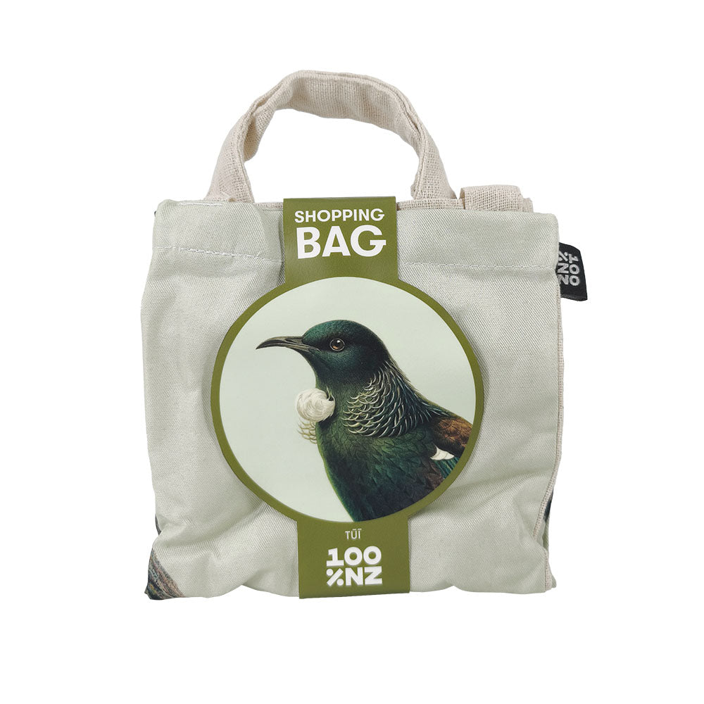 The Hushed Tui Shopping Bag is a reusable white bag with short handles, featuring a circular bird illustration labeled SHOPPING BAG and a black side tag. Its an affordable, eco-friendly choice for your shopping needs.