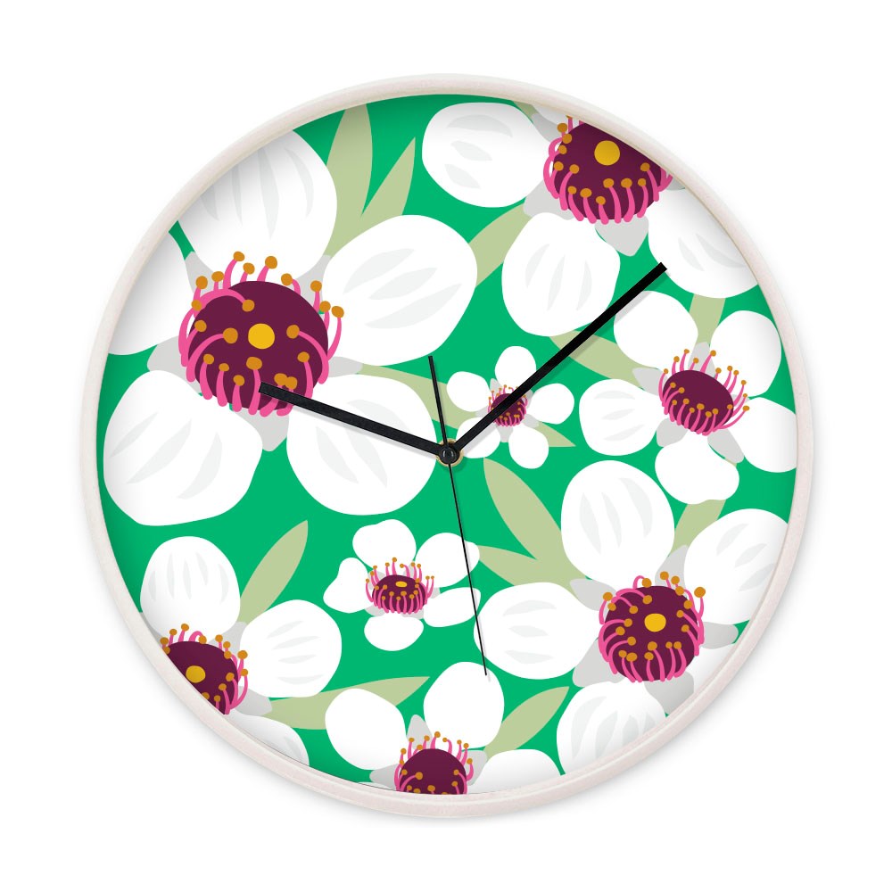 The Bright Botanical Manuka Wooden Frame Clock features a silent movement and a green background with white flowers, dark pink centers, and yellow accents—a vibrant design inspired by New Zealand’s natural beauty.