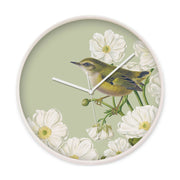 The Rifleman Wooden Frame Clock, made in New Zealand, has a round design with a white wooden frame and glass front. It features an illustration of a small bird on white flowers with a light green background and has white hour, minute, and second hands.