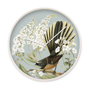 The Fantail and Fiordland Parahebe Wooden Frame Clock features a glass front, white hands, and an illustration of a brown fantail bird among white flowering plants on pale blue, inspired by New Zealand’s natural beauty.