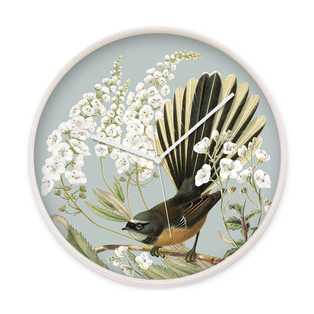 The Fantail and Fiordland Parahebe Wooden Frame Clock features a glass front, white hands, and an illustration of a brown fantail bird among white flowering plants on pale blue, inspired by New Zealand’s natural beauty.