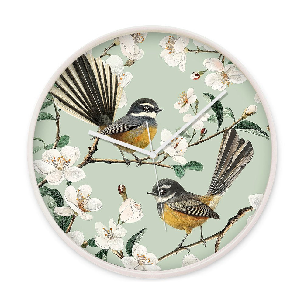 The Chatty Fantails Wooden Frame Clock features a round pale wooden frame with two yellow and gray NZ Fantails perched on flowering branches with white blossoms, set against a light green background.