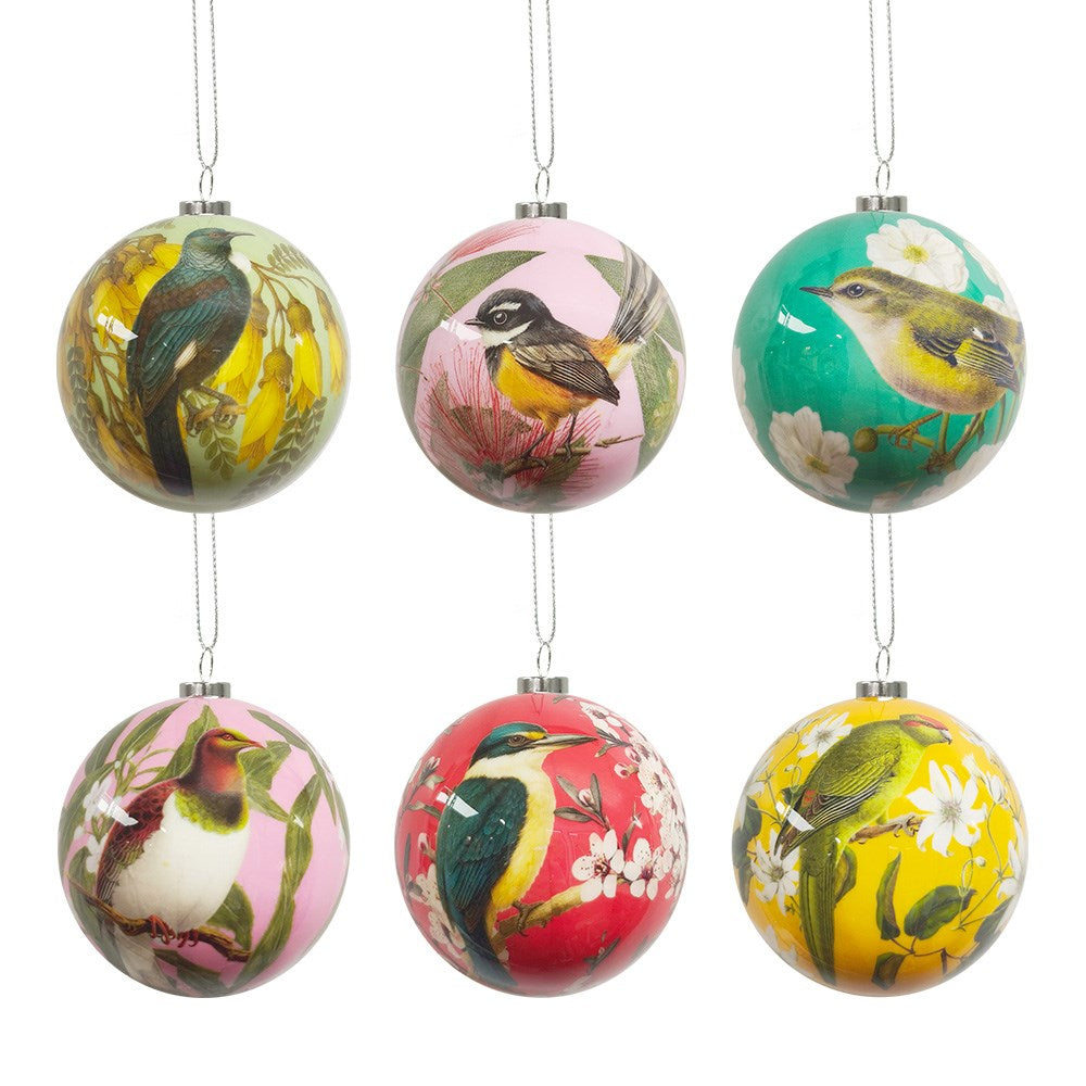 The NZ Native Birds Christmas Baubles boxset includes six round ornaments, each decorated with colorful illustrations of native birds and flowers in green, pink, and red, and finished with a delicate silver hanging string.