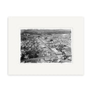 Black and white aerial photograph titled Pukekohe 1946 - HI196 shows a small town with houses, buildings, and roads amid open countryside. This historical print is mounted with a wide white mat.