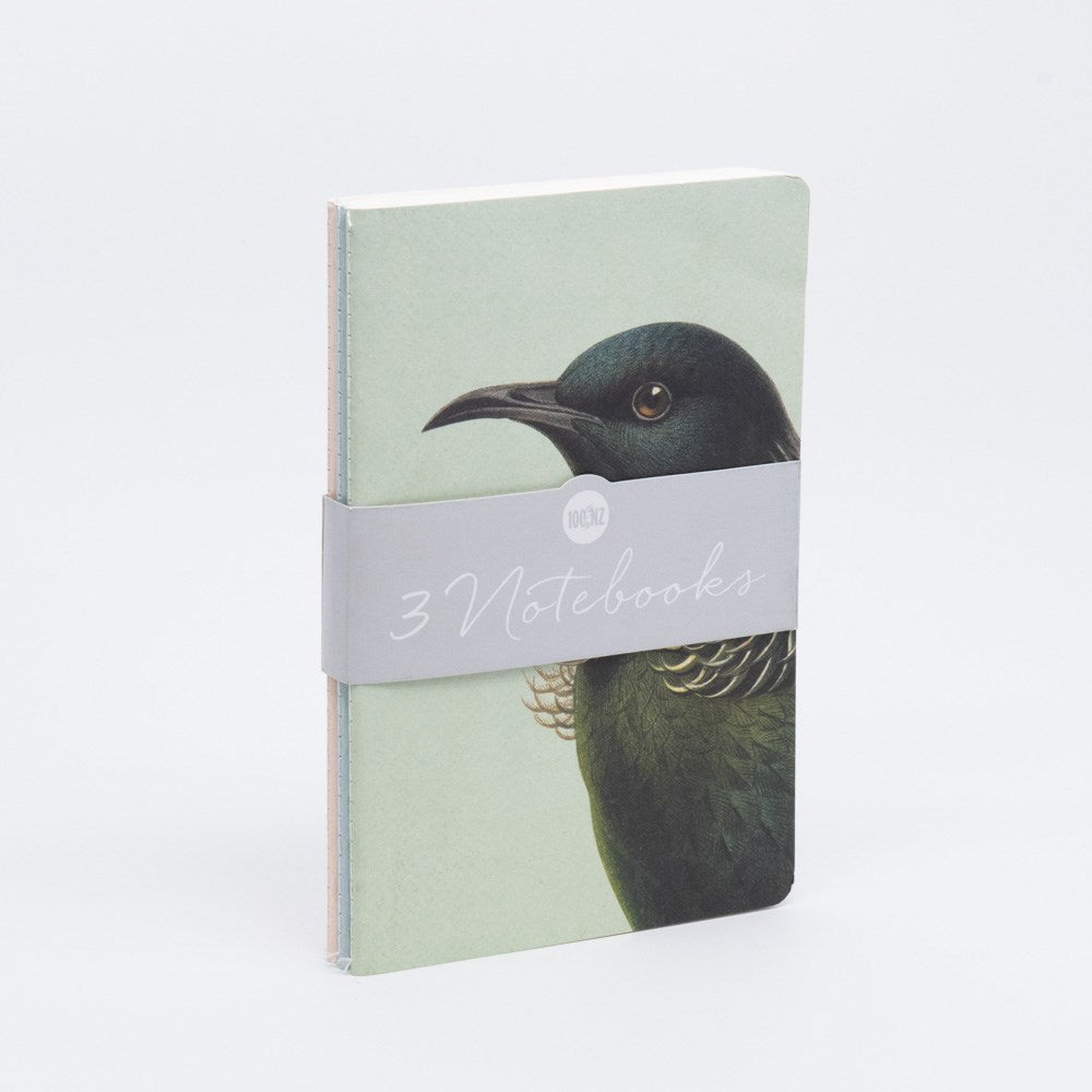 The Hushed Birds Notebook Set includes three hand-stitched notebooks, bound with a gray band labeled 3 Notebooks. The front cover displays an illustration of a dark-feathered bird against a pale background.
