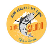 The NZ Seafood Salmon Frameless Clock is round and yellow, showing a leaping salmon before white mountains with New Zealand Mt Cook, Alpine Salmon, Rich and Smooth text. Black silent hands complete this New Zealand-inspired design.