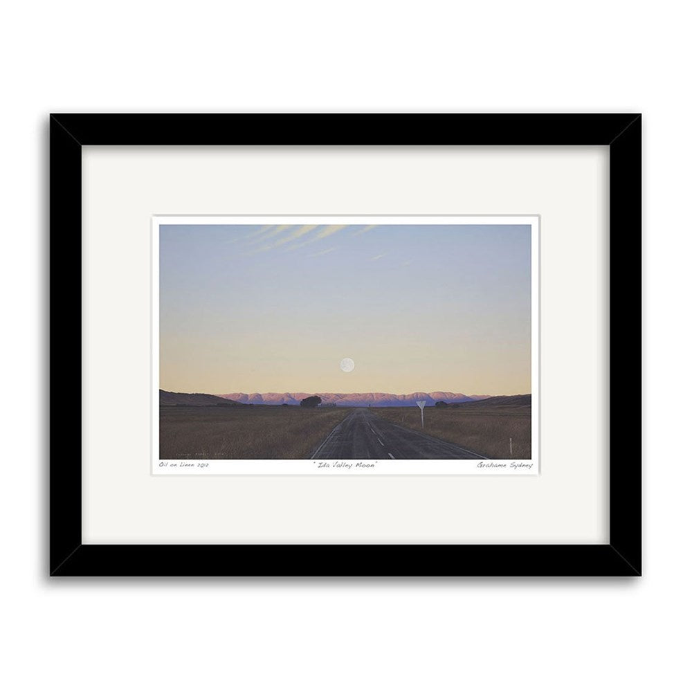 The Grahame Sydney - Ida Valley Moon Small Art Print: Second Frame features a serene landscape with an empty road, distant mountains, and the moon near the horizon under a pale sky. Limited edition available.