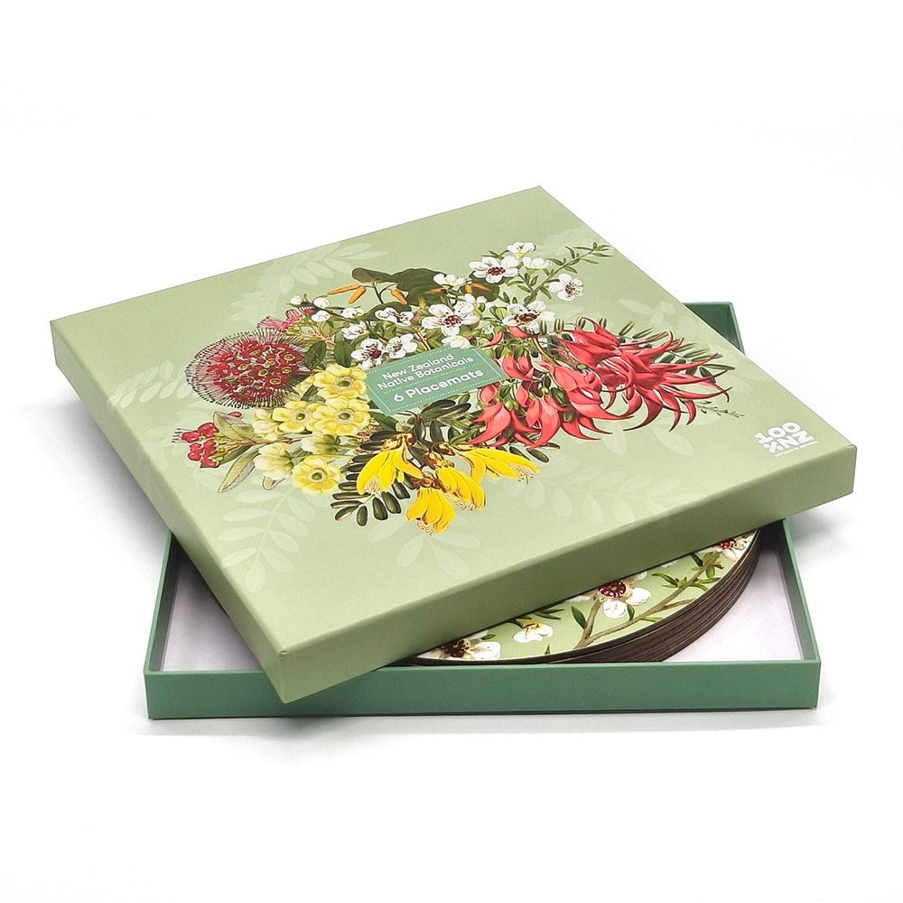 A partially open box labeled NZ Native Botanicals reveals cork-backed placemats inside. The lid has colorful illustrations of native flowers and the name NZ Native Botanicals on a green background.