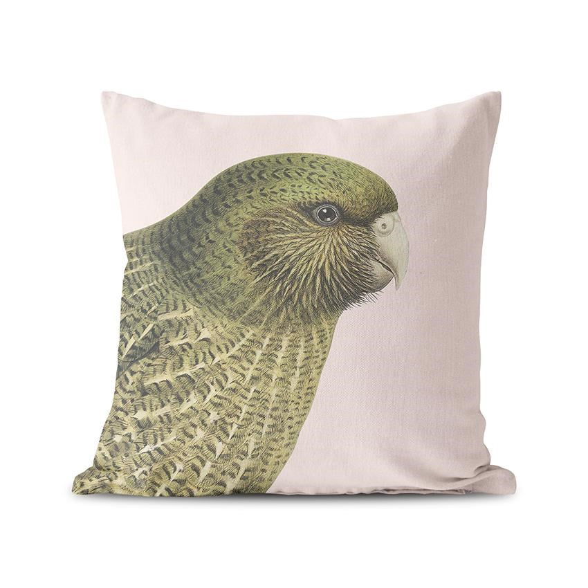 The Hushed Pink Kakapo Cushion Cover features a detailed illustration of a green New Zealand native parrot with realistic feathers on a light beige microfibre suede-feel square pillow cover.