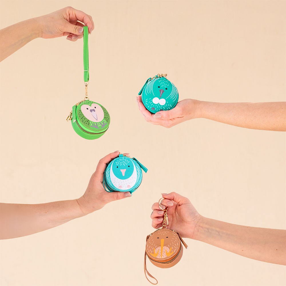 Four hands hold Kereru Cutie Coin Purses in green, teal, and brown. Each features an animal face with a keychain or wrist strap—a stylish pick for fashion lovers displayed on a neutral beige background.