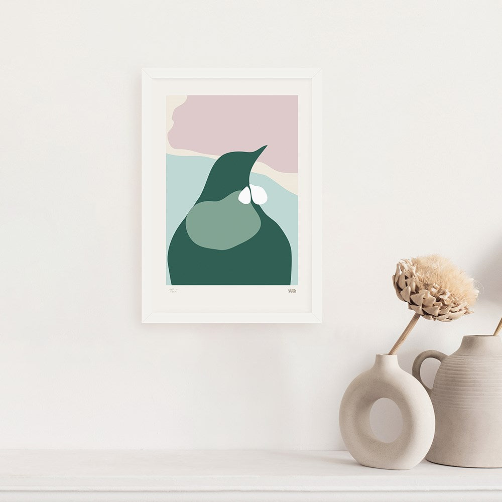 The Modern Tui Print, a minimalist artwork with fluid green, pink, and beige abstract shapes in a sleek frame, hangs on a white wall above a shelf displaying neutral ceramic vases and dried flowers.