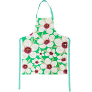 The Bright Botanical Manuka Apron is made of 100% cotton and features a vivid green background with large white flowers, purple and yellow accents, teal straps, and is inspired by vibrant New Zealand design.