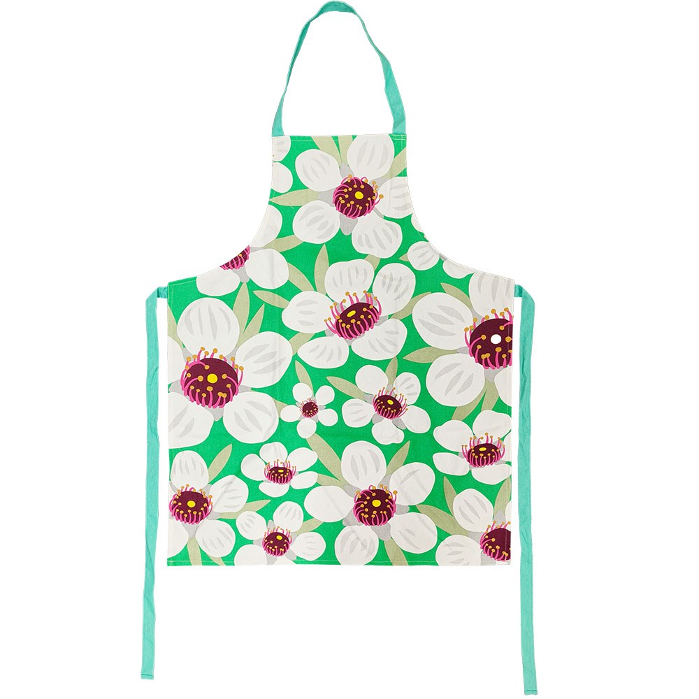 The Bright Botanical Manuka Apron is made of 100% cotton and features a vivid green background with large white flowers, purple and yellow accents, teal straps, and is inspired by vibrant New Zealand design.