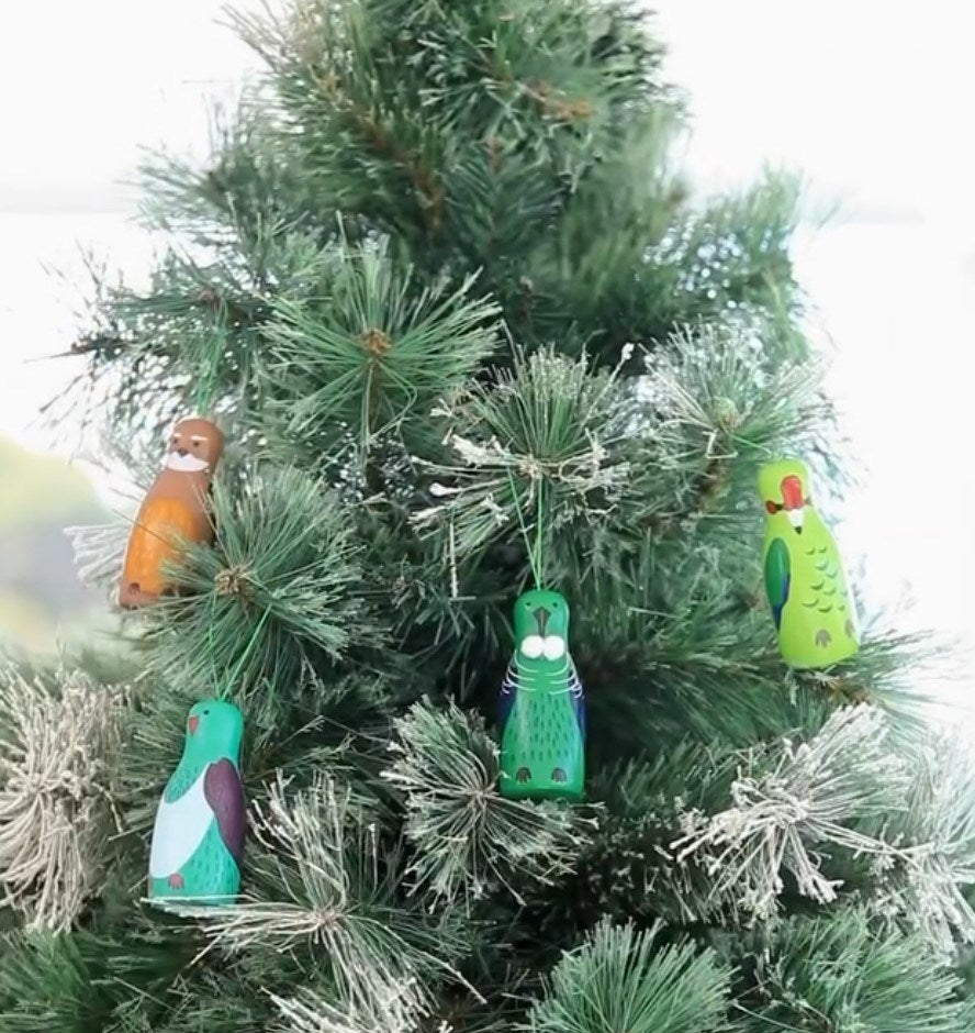 A green artificial Christmas tree displays four colorful New Zealand Native Bird ornaments from the limited Box of Native Bird Ornaments - Seconds set, each resembling a different native species and hanging among the branches.