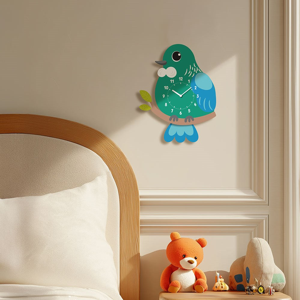 A Tui Kids Wobble Clock hangs above a wooden bed with a white pillow. An orange teddy bear and plush toy sit on a small table against a beige paneled wall below the clock.