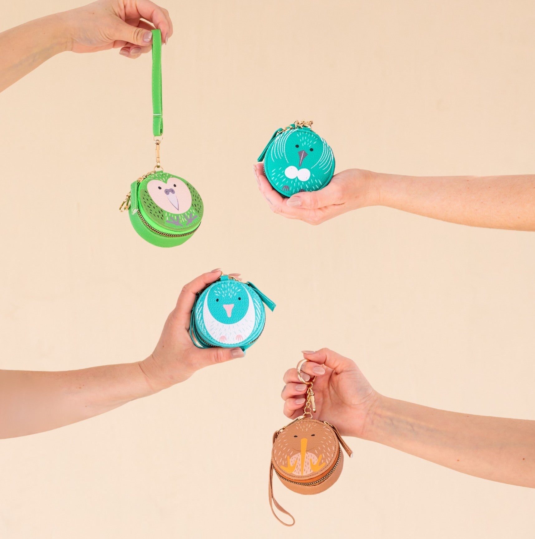 Four hands hold out small, circular Kakapo Cutie Coin Purses with playful animal faces against a beige background. Perfect for fashion lovers, the green purses each showcase a unique kakapo bird design.
