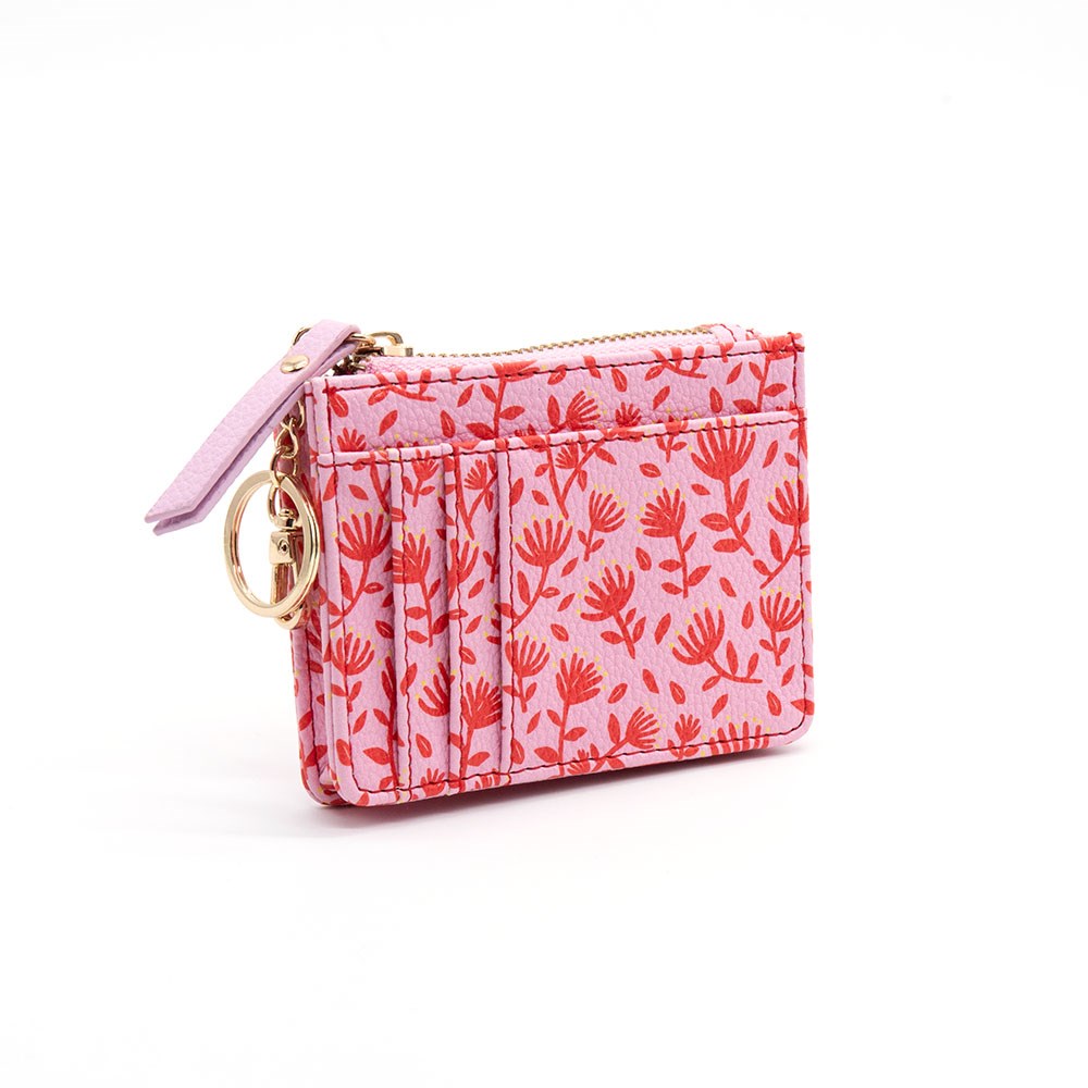 The Pohutukawa Pattern Coin Purse is a small pink vegan leather accessory with a red floral design, gold keyring, and lilac zipper pull, shown standing upright on a white background.