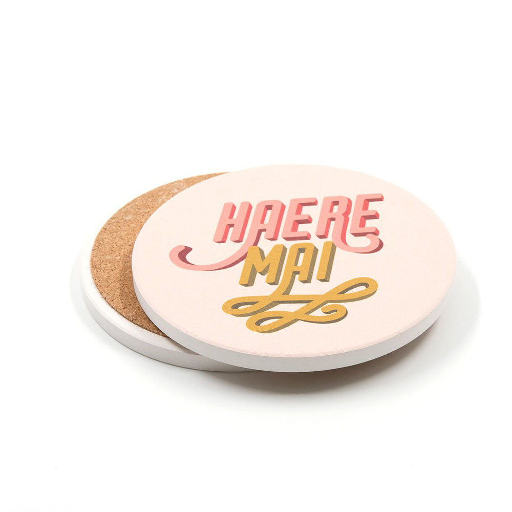 A set of 4 ceramic coasters with cork backing and a white top, featuring vibrant pop art Te Reo designs like "HAERE MAI" in pink and yellow. New Zealand-themed, perfect for adding color to your table.