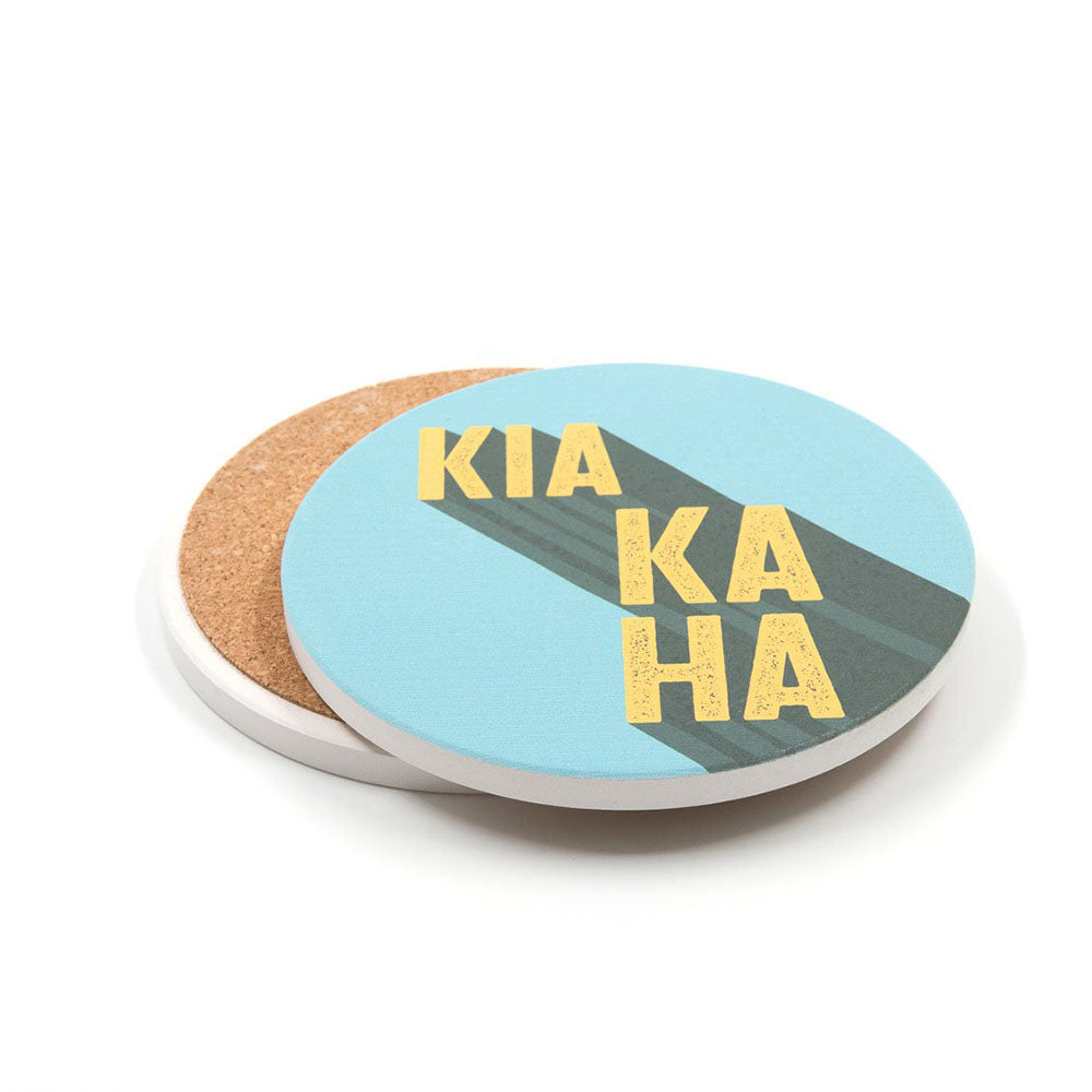 Set of 4 Te Reo Ceramic Coasters: round pop art coasters with blue tops and yellow “KIA KAHA” Te Reo typography, plus plain cork undersides—a vibrant nod to New Zealand style.