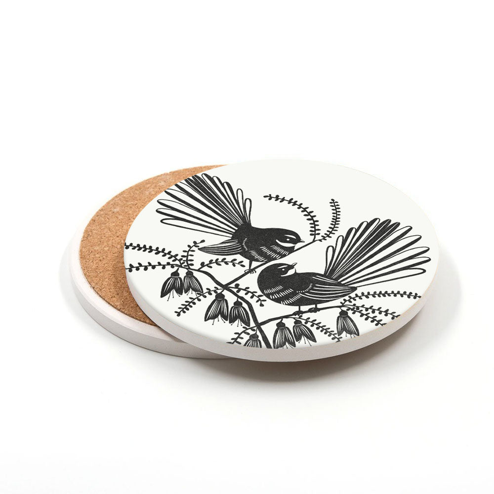 This set of 3 ceramic coasters with cork backing showcases black and white linocut-style illustrations of two birds on flowering branches, inspired by New Zealand, all on a crisp white background.