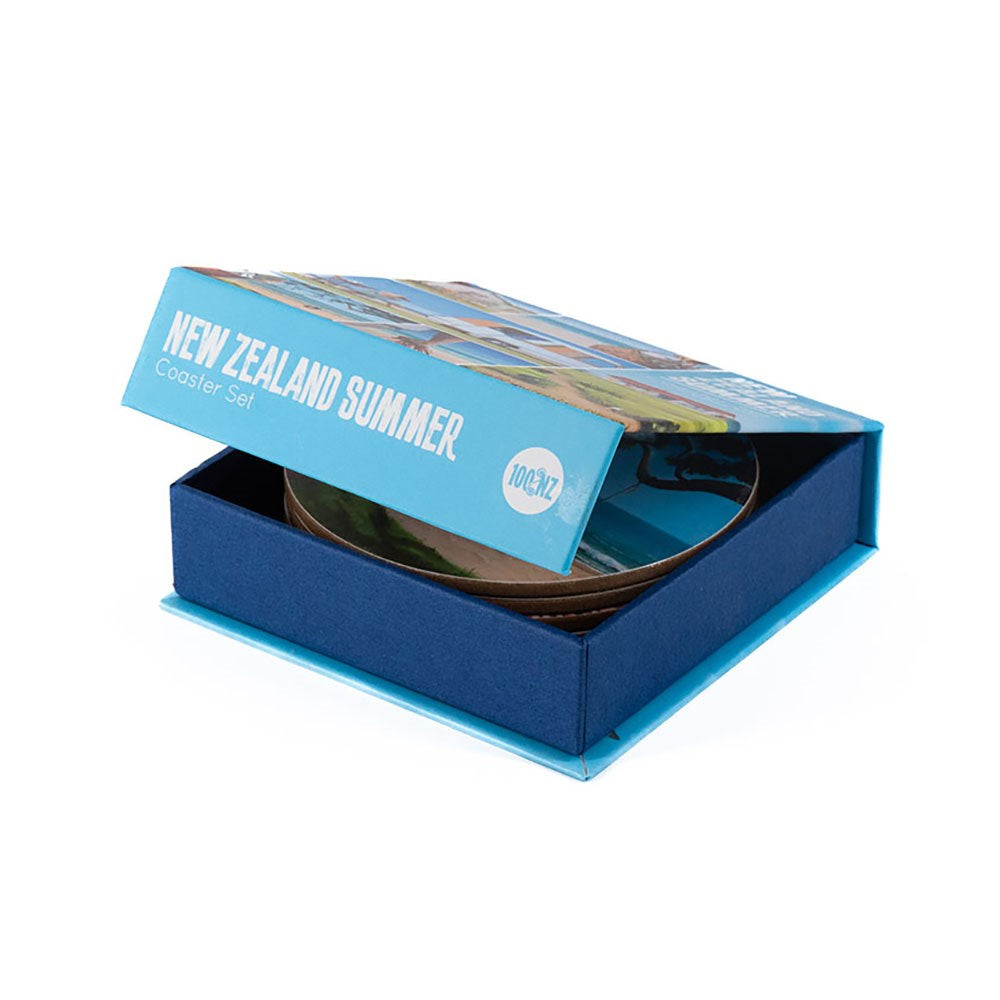 A partially open blue box labeled Graham Young NZ Summer Set of 6 Coasters reveals round coasters inside. Perfect for beach lovers, the box features landscape artwork and the text 100% NZ on the lid.