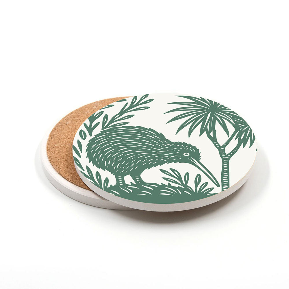 A round ceramic coaster from the Set of 4 Woodcut Ceramic Coasters features a green kiwi bird and foliage in a woodcut style on white, with a cork base. Printed in New Zealand, one coaster is partially resting on another identical one.