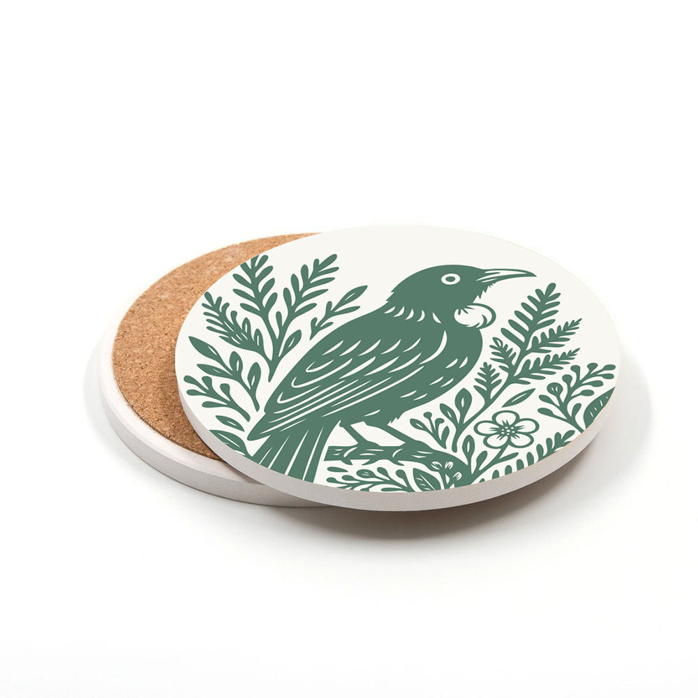 The Set of 4 Woodcut Ceramic Coasters features round ceramic coasters with cork bases and white surfaces, each printed in New Zealand with a green woodcut-style bird among leafy branches and flowers.