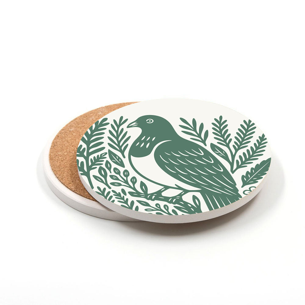 The Set of 4 Woodcut Ceramic Coasters features a round ceramic design with cork bases, showing a green bird among leafy branches in woodcut style on a crisp white background. Printed in New Zealand.