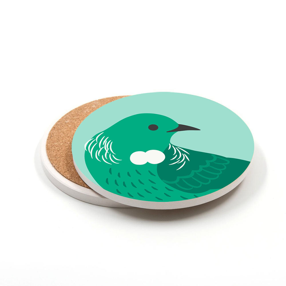 Part of the Set of 4 Storybook Ceramic Coasters, this round ceramic coaster, printed in New Zealand, shows a green bird with a white neck mark on a light teal background and is partially stacked on another coaster.