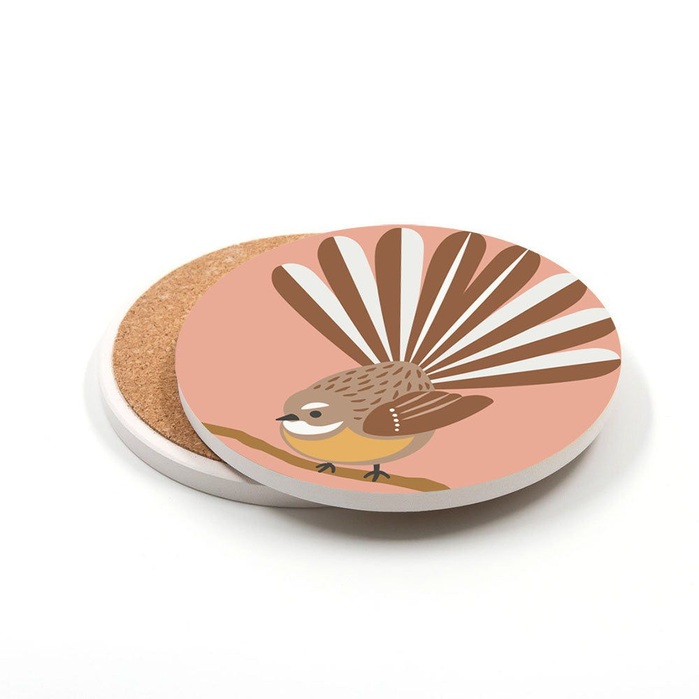 A Set of 4 Storybook Ceramic Coasters features a round ceramic coaster with a cork backing, illustrated with a brown New Zealand fantail bird perched on a branch against a peach background. Another coaster peeks out behind it.
