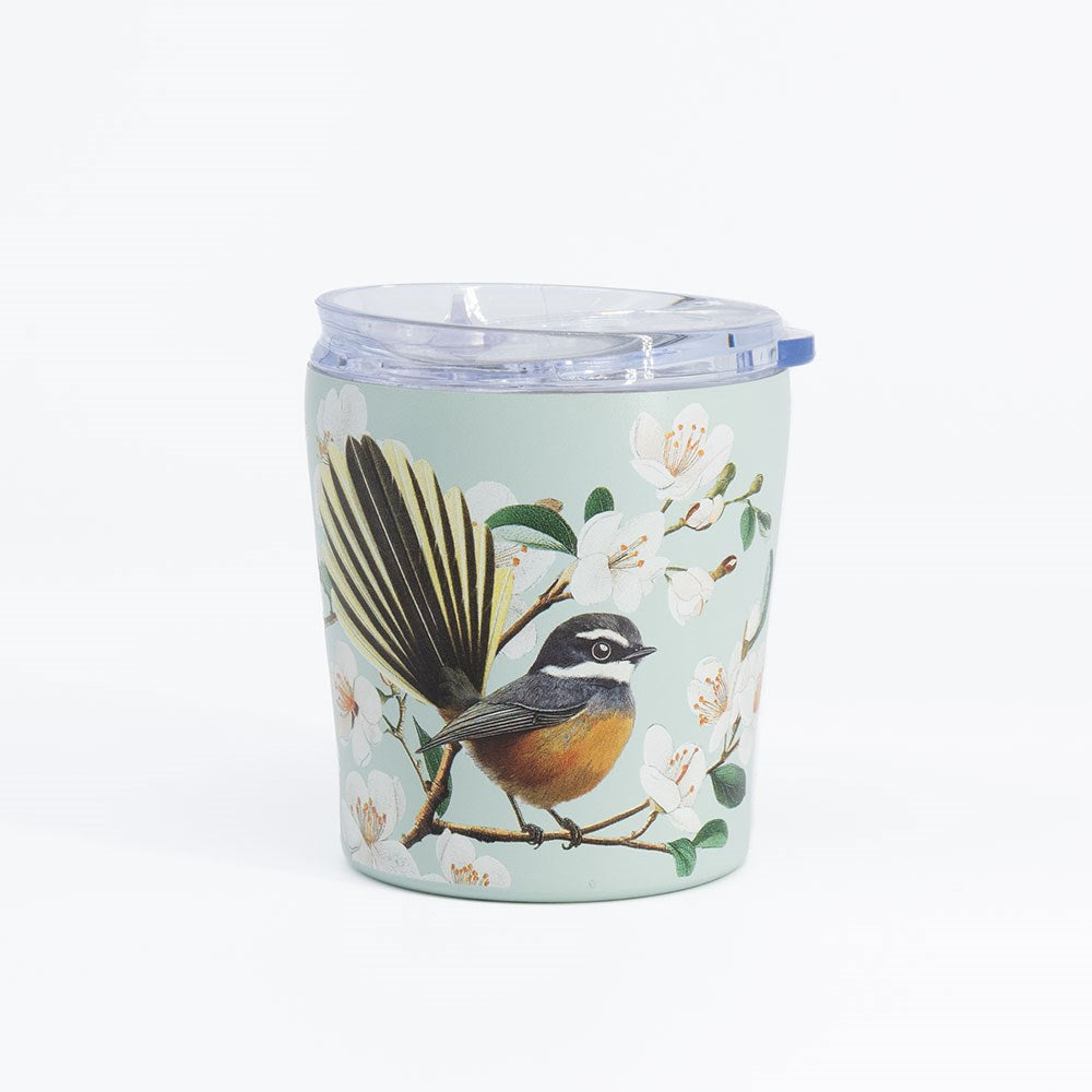 A light green, vacuum insulated Chatty Fantail Coffee Cup with a clear lid, featuring an illustration of a small bird perched on a branch adorned with white flowers and green leaves.