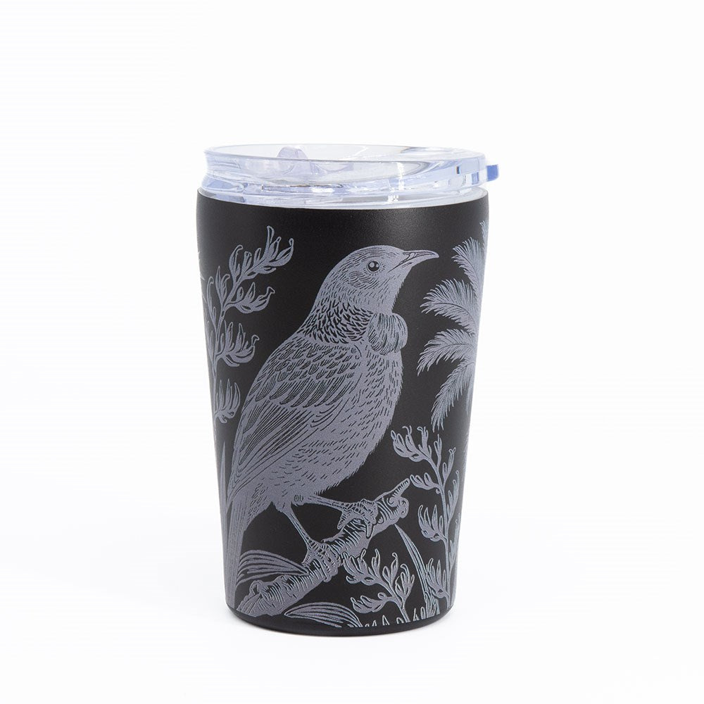 The Midnight Tui Coffee Cup is a black stainless steel travel mug with a clear plastic lid, featuring a detailed illustration of a tui bird perched on a branch amid leaves and foliage. The nature-inspired design is etched in light gray, while the spill-resistant, vacuum insulated construction keeps your drinks hot or cold in style.