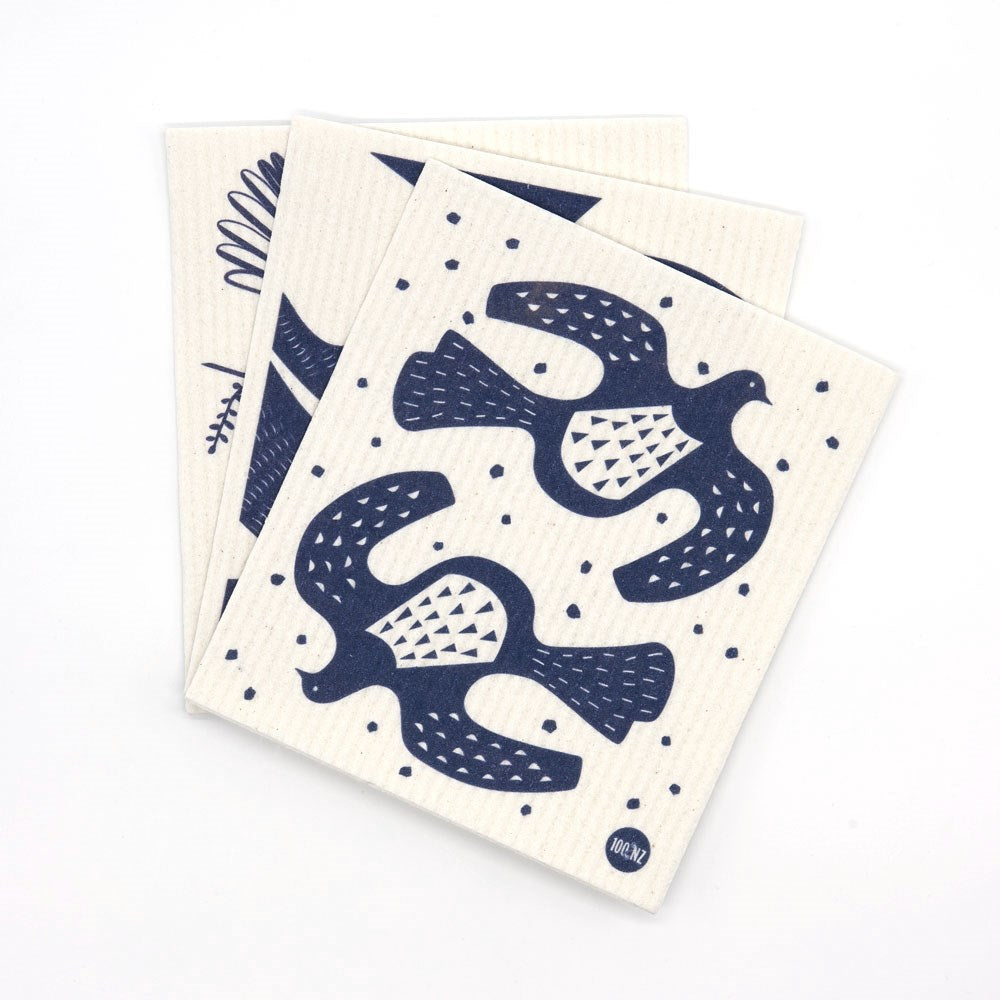 Three eco-friendly Swedish Dishcloths - Linocut with blue designs are stacked on a white background. The top cloth shows two stylized birds, while hints of Kiwiana imagery can be seen on the other two underneath.