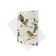 The Chatty Fantails Gift Card & Envelope (6 Pack) features two New Zealand native Fantails with yellow and gray feathers on flowering branches, set against a pale background—perfect for your personalised message.