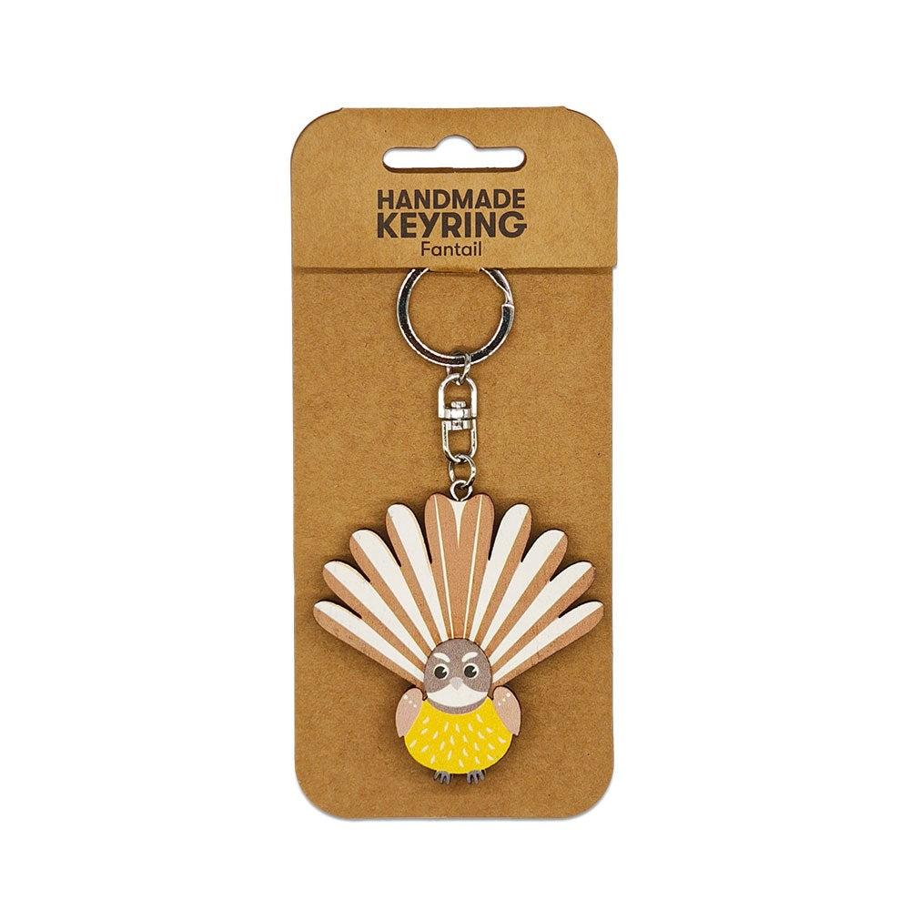 The Fantail Wooden Keyring features a fantail bird with spread tail feathers, attached to brown card packaging labeled HANDMADE KEYRING Fantail—a charming, handmade Kiwi-themed keychain and unique accessory.