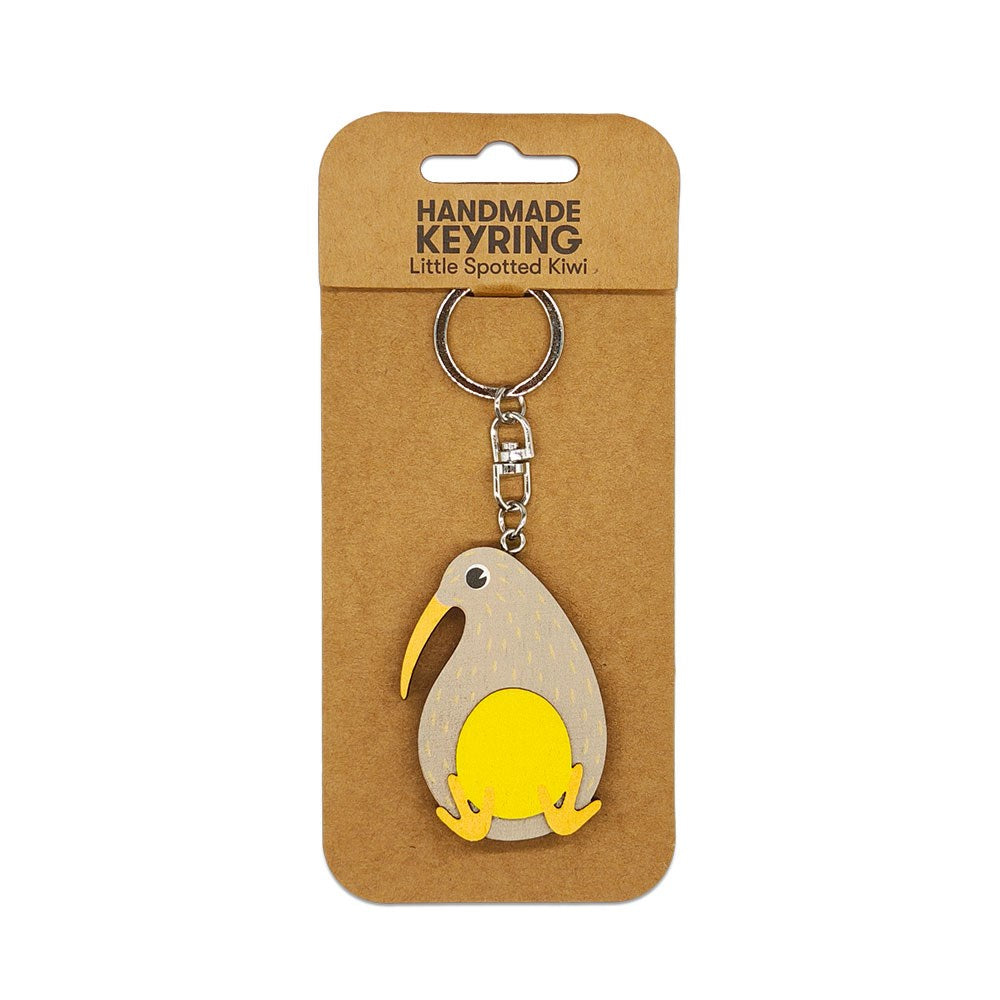 The Little Spotted Kiwi Wooden Keyring is a handmade wooden keychain shaped like a stylized kiwi bird with a yellow beak and feet, attached to a metal ring—an ideal Aotearoa keepsake displayed on HANDMADE KEYRING packaging.