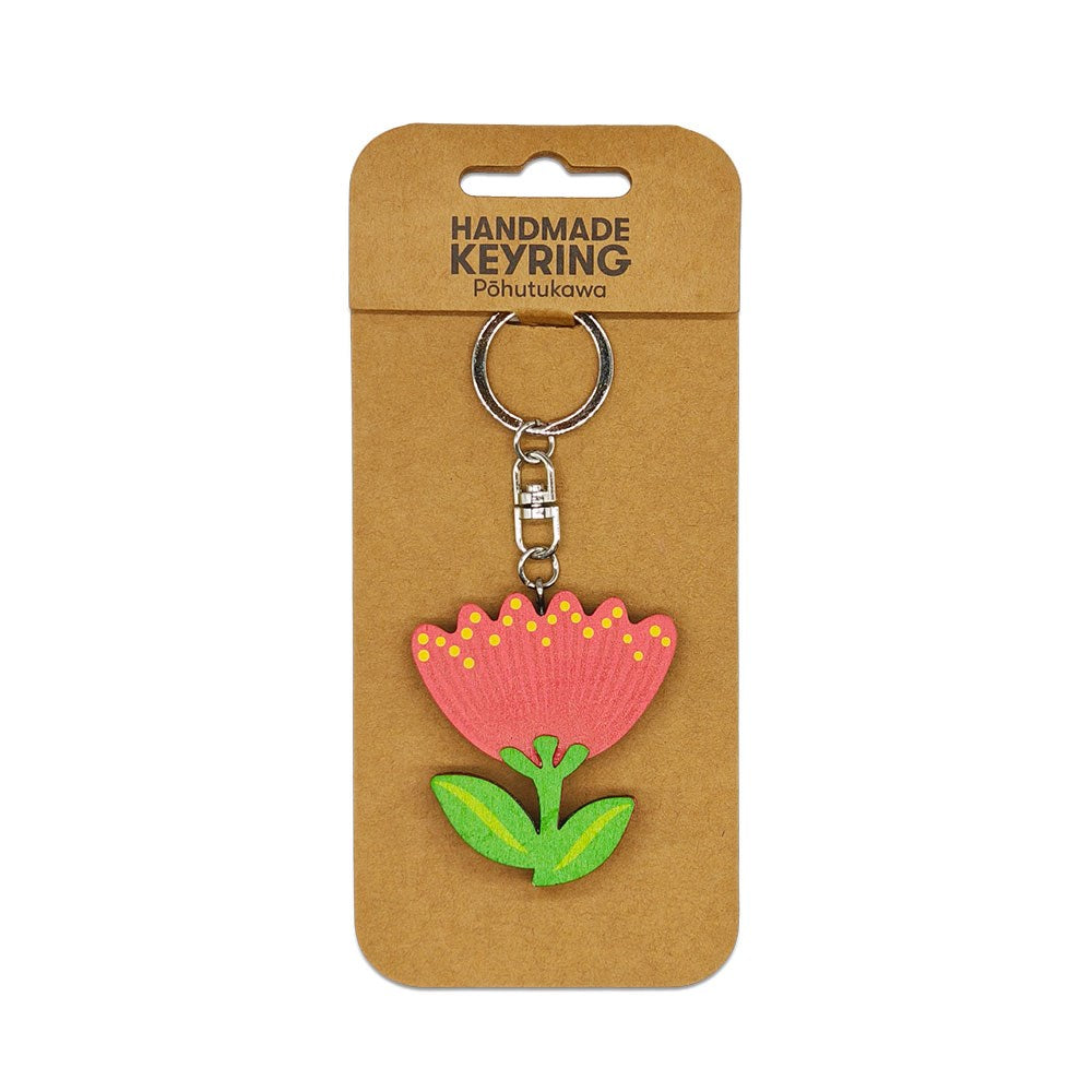 The Pohutukawa Wooden Keyring is a handmade wooden keychain with a red and pink stylized pohutukawa design, yellow dots, and green leaves, attached to a brown backing card labeled Handmade Keyring Pōhutukawa.