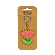 The Pohutukawa Wooden Keyring is a handmade wooden keychain with a red and pink stylized pohutukawa design, yellow dots, and green leaves, attached to a brown backing card labeled Handmade Keyring Pōhutukawa.