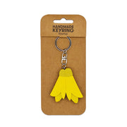 A Kowhai Wooden Keyring, shaped like a yellow flower and handmade from wood, is attached to a metal keychain and displayed on brown cardboard labeled HANDMADE KEYRING Kowhai.