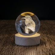 The Kingfisher LED Globe features a glass sphere with a 3D laser-engraved kingfisher, displayed on a round wooden base and illuminated from below, creating a stunning effect against a dark background.